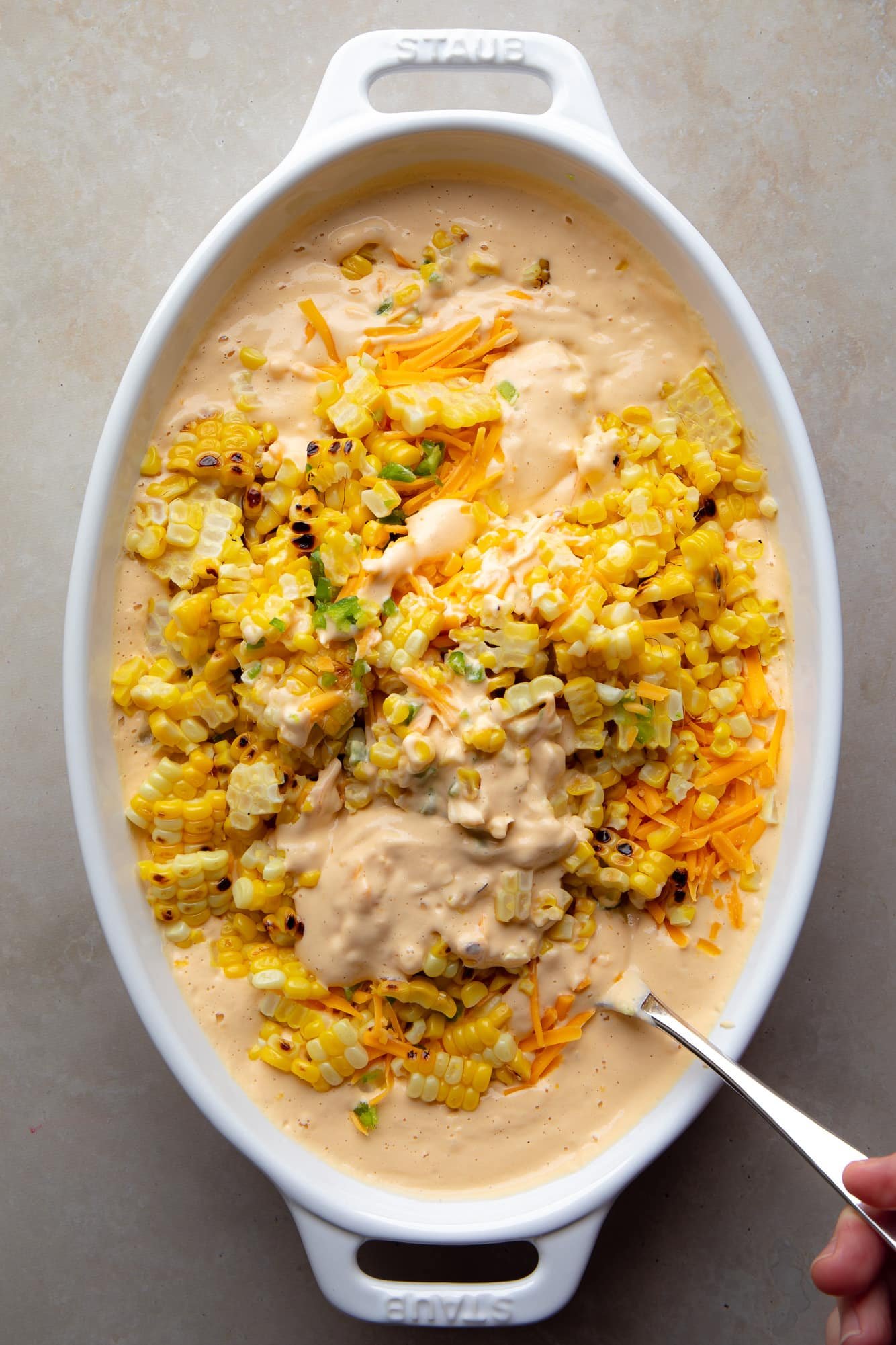 Use a spoon to combine the ingredients for vegan Mexican corn immersion with a creamy anacard sauce on a cooking dish.